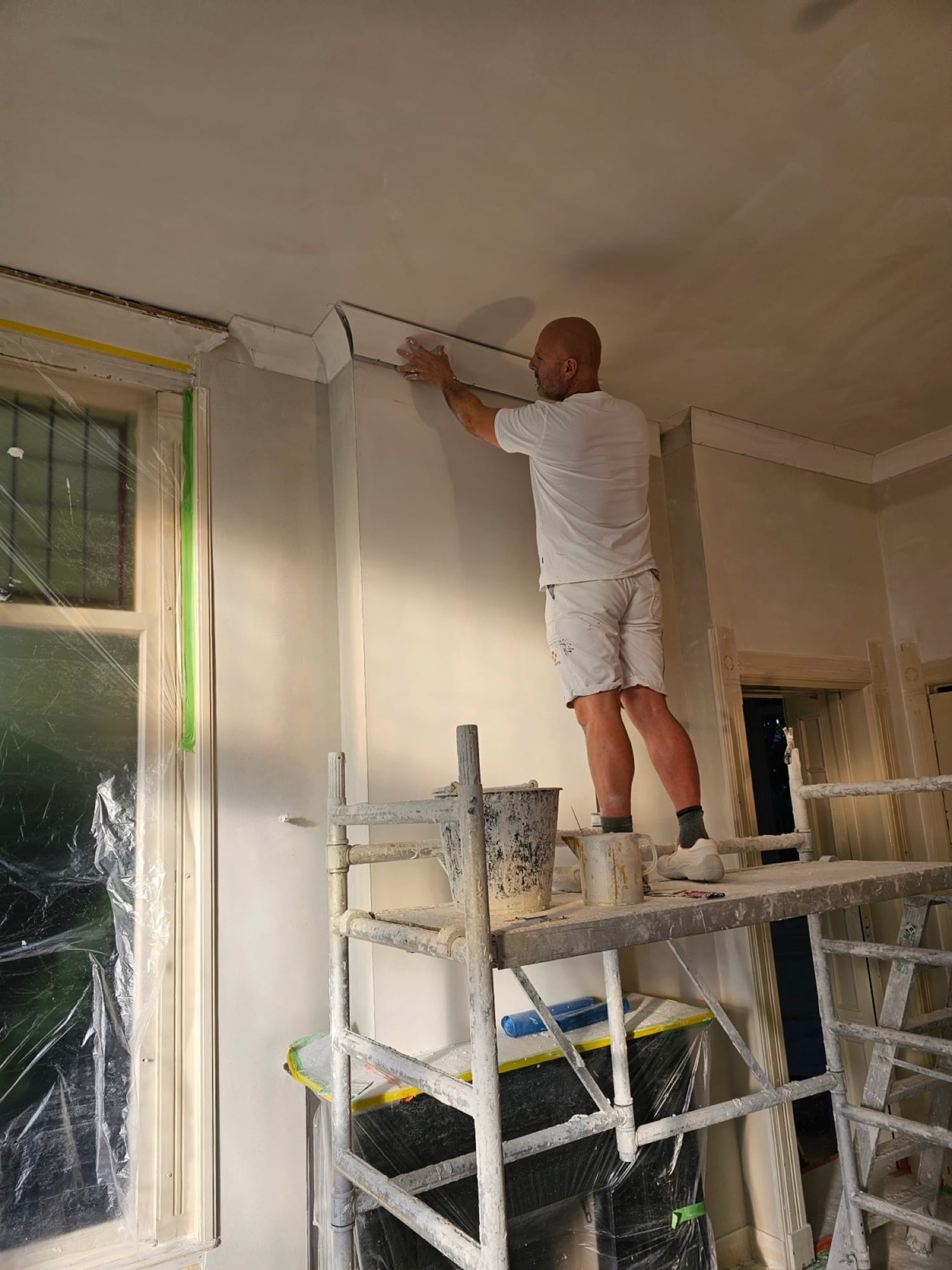 Stukadoor werkt vanaf de steiger de kroonlijst langs het plafond strak af